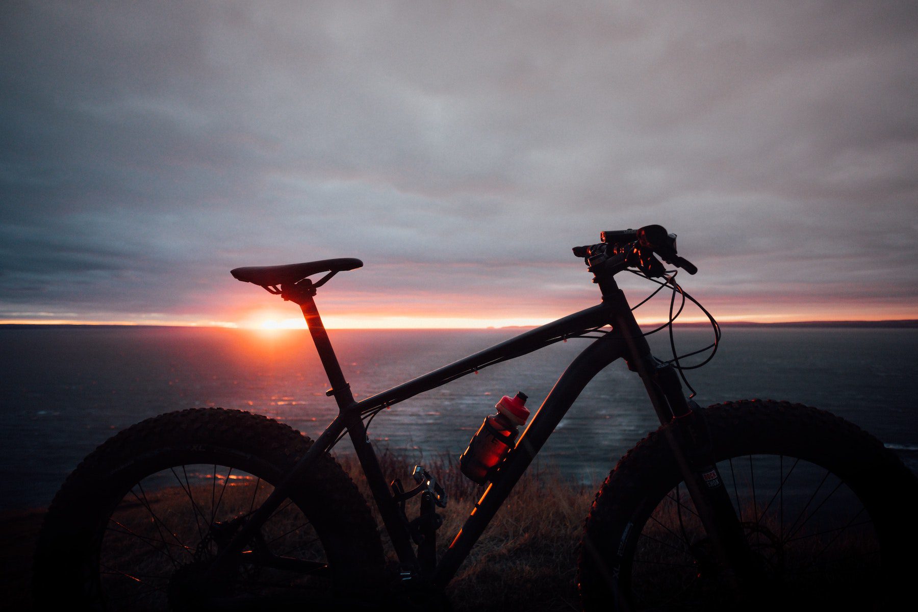 Silhouette of a bicycle against a pink and gray sunset atop a mountain.